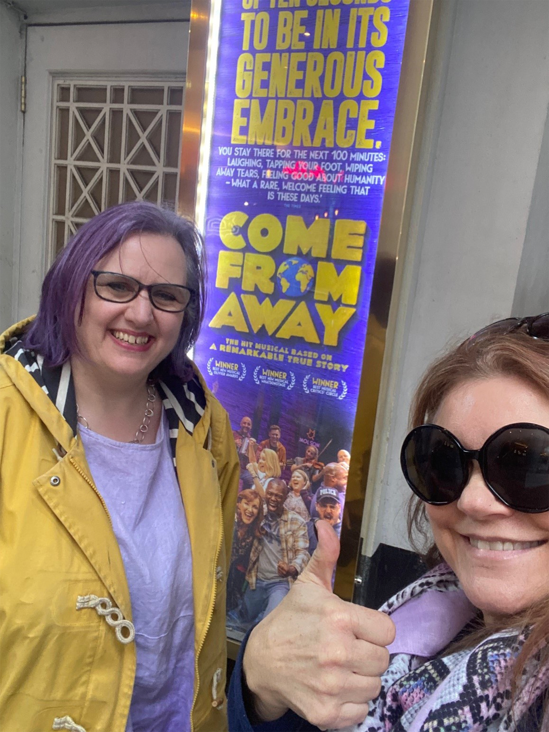 Debbie and a friend stood in front of a sign for the musical Come From Away 