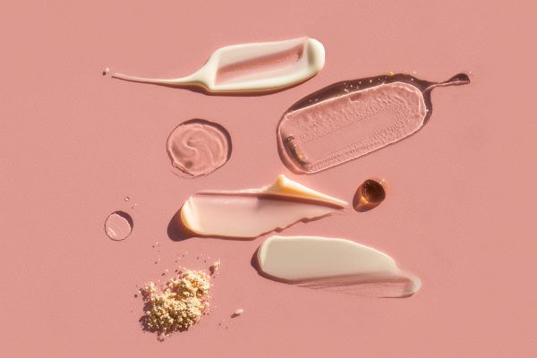 Closeup strokes and drops of assorted moisturizing cosmetic products spread on pink background. Good for your design