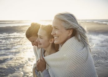 Grandmother, mother and daughter wrapped in a blanket on the beach